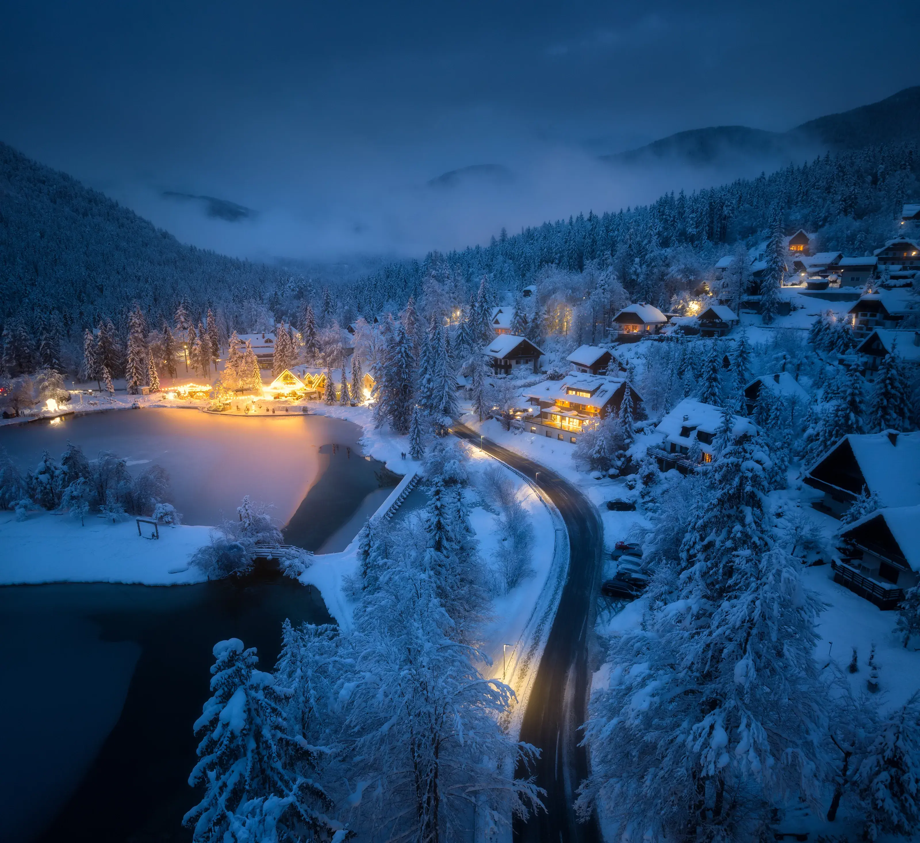  Comp Image Aerial view of fairy town in snow, road, forest, Jasna lake and houses with lights at night in winter.