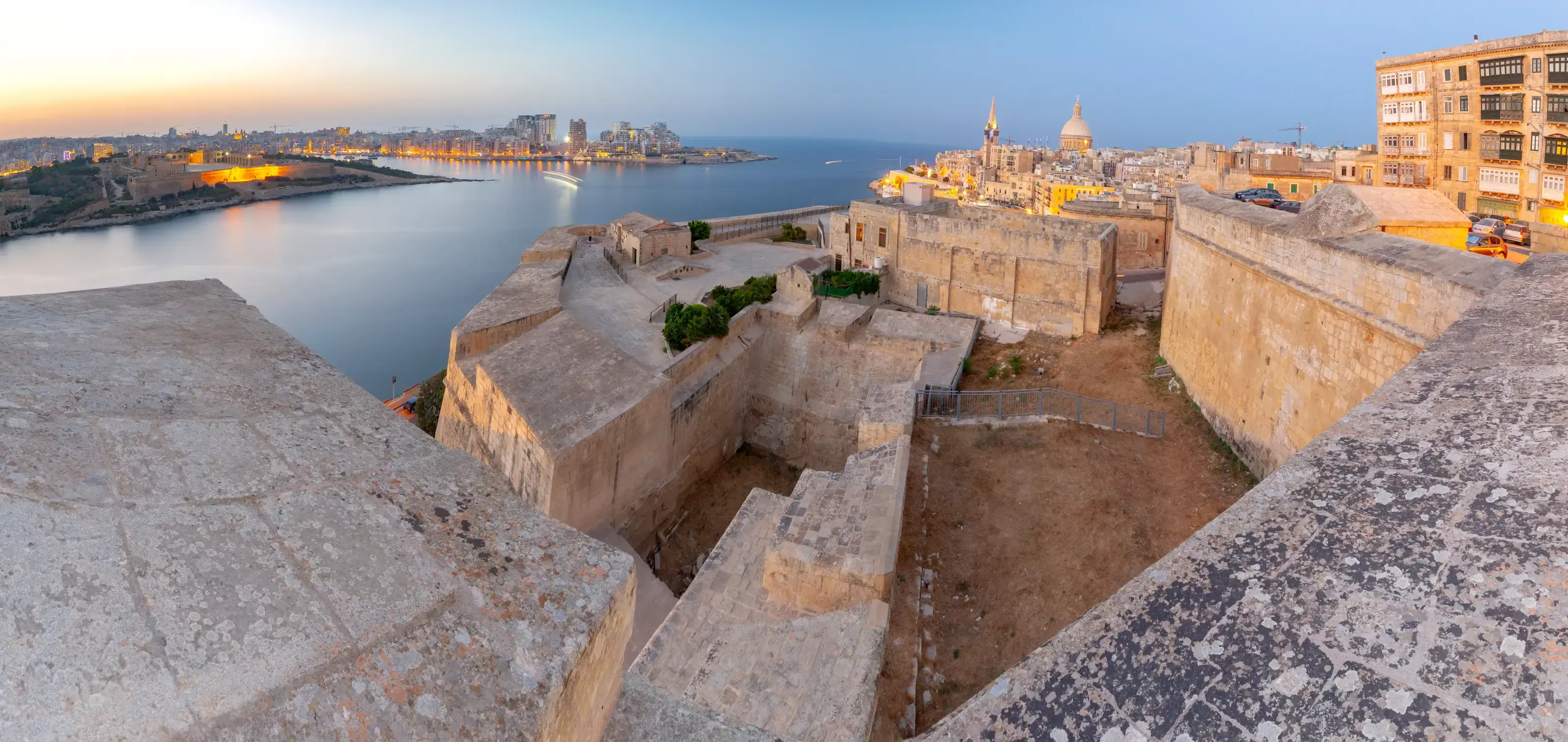 Panoramic views of the medieval city fortifications and the bay at sunset. Valletta. Malta.. Malta. Panorama of the old harbor at sunset.