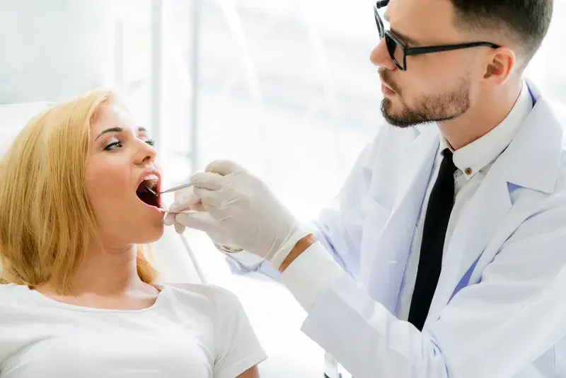 Young dentist examining teeth of happy woman patient sitting on dentist chair in dental clinic. Dentistry care concept.