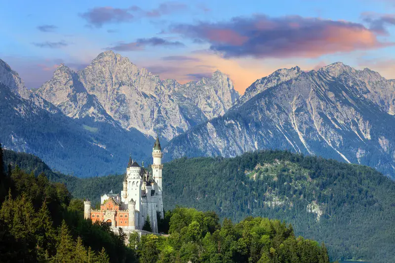 The iconic Neuschwanstein Castle in Bavaria, Germany, set against the dramatic backdrop of the soaring Alps at sunset.