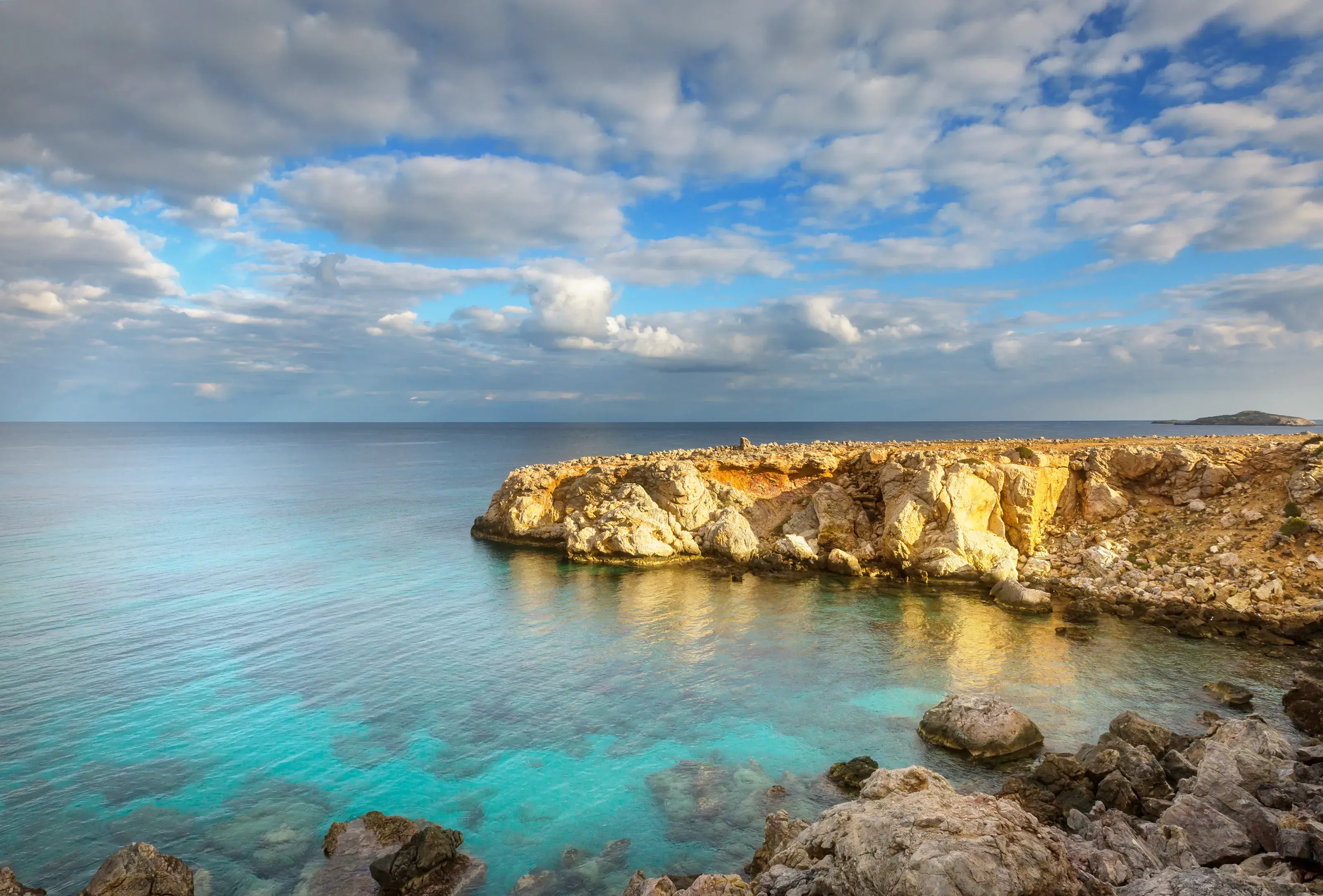 A tranquil scene of a rugged, rocky Northern Cyprus coastline meeting the calm, crystal-clear turquoise sea under a dramatic blue sky