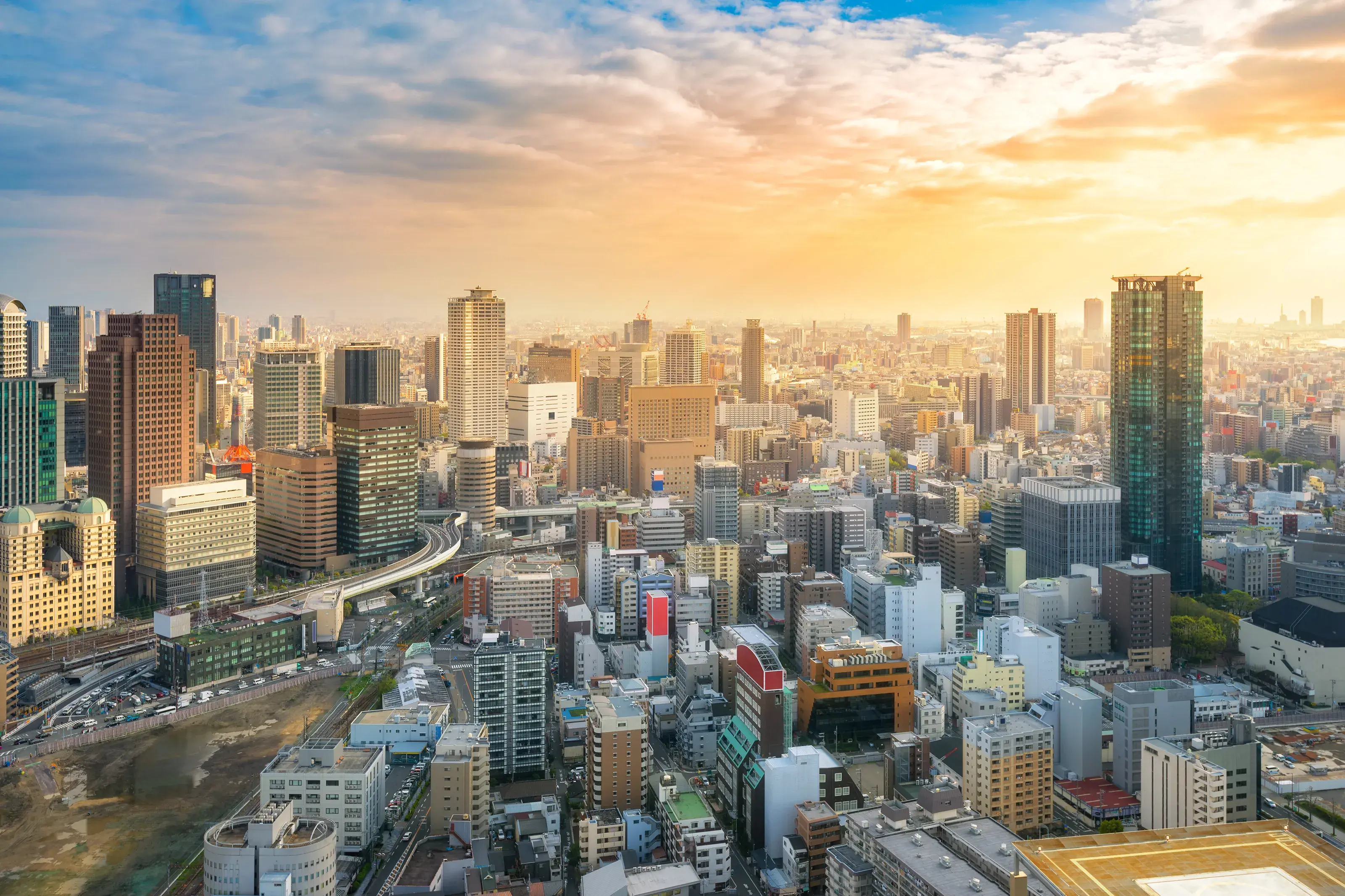 A sprawling aerial view of the dense Osaka city skyline in Japan, bathed in the warm glow of sunset.