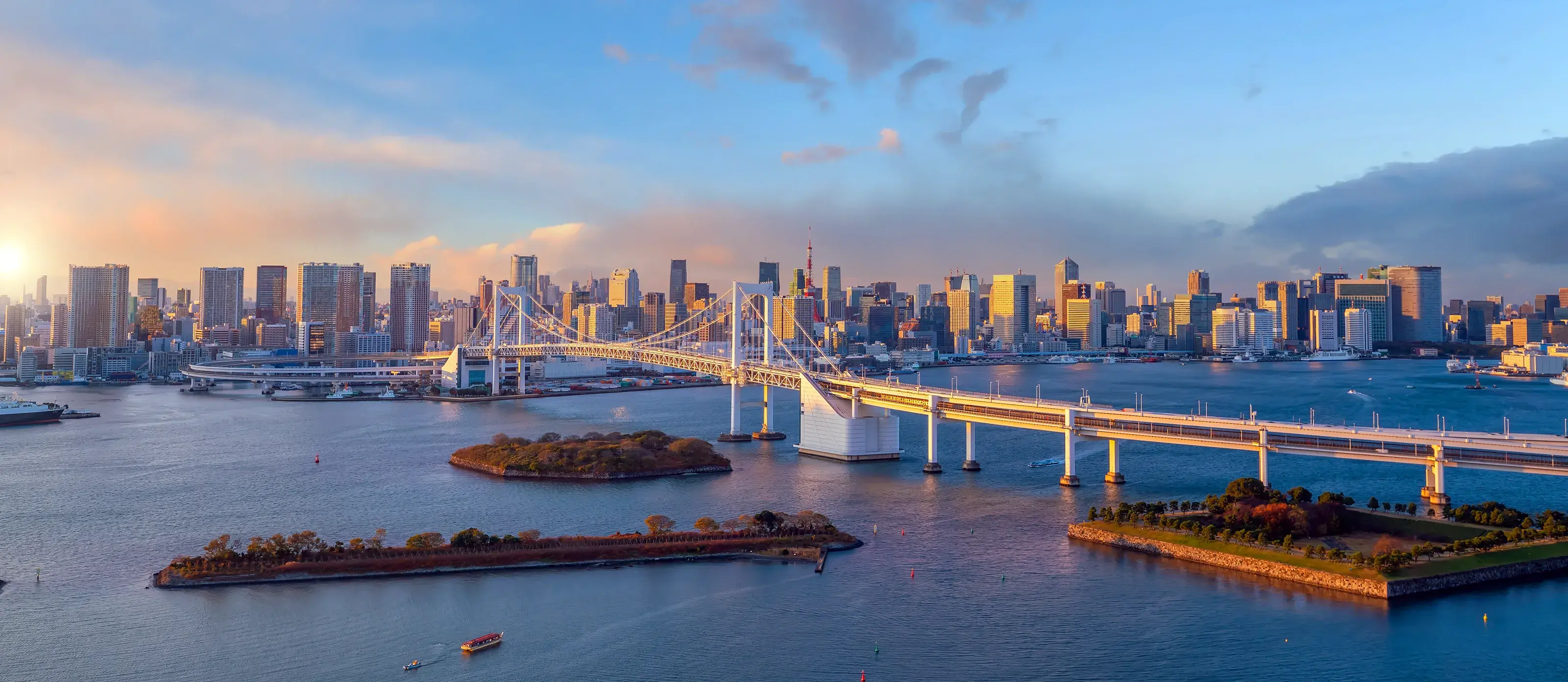 A stunning panoramic view of the Tokyo skyline and the Rainbow Bridge over Tokyo Bay at sunset.